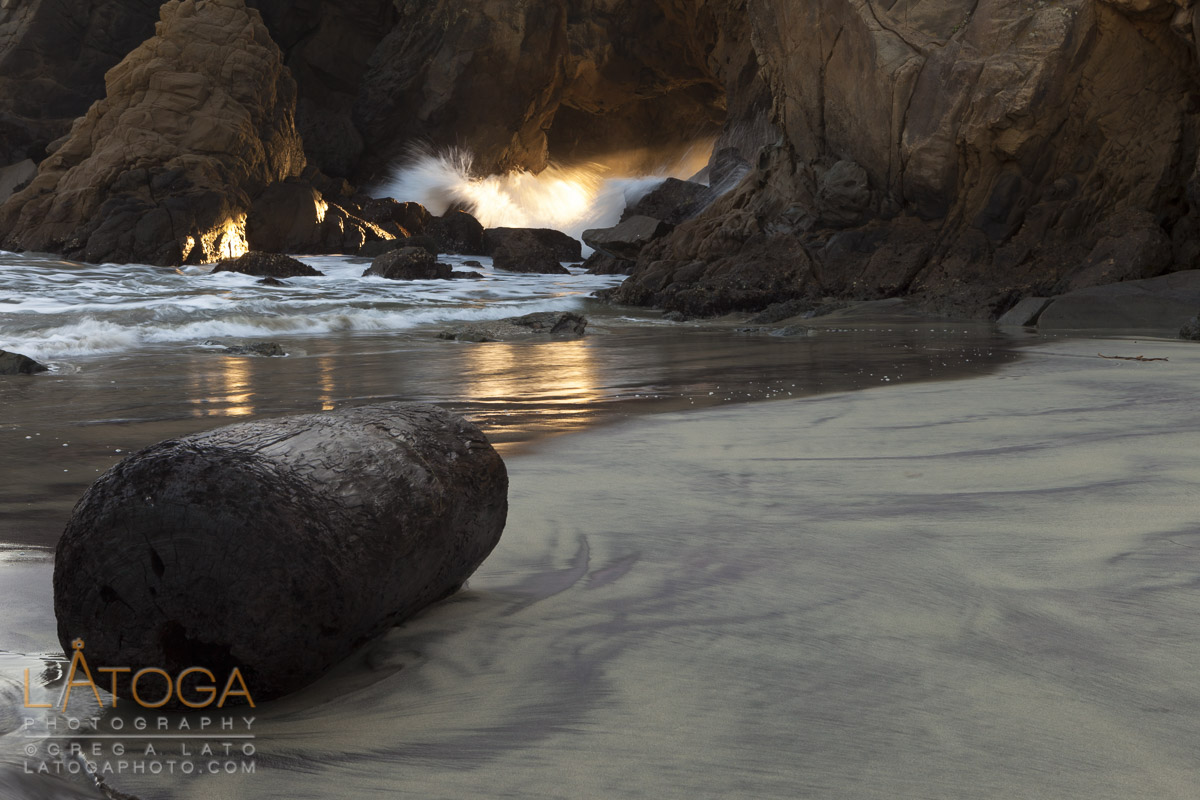 A water soaked log witnesses sunset streaming through a sea arch at Pfeiffer Beach, Big Sur, California.