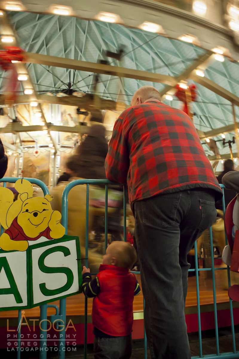 Little boy and adult man standing side by side watching a carousel at Tilden Regional Park in Berkeley, California.